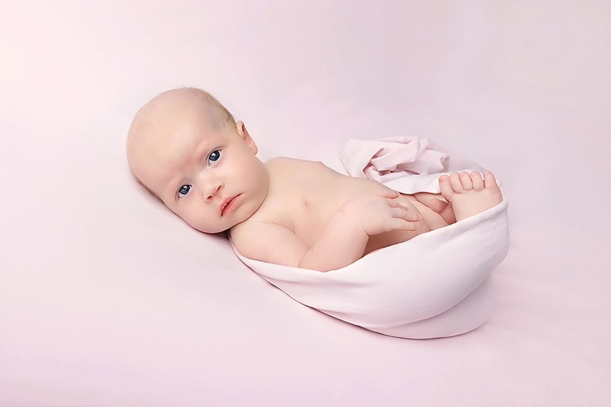 Meisje geposeerd op roze kleed tijdens babyshoot